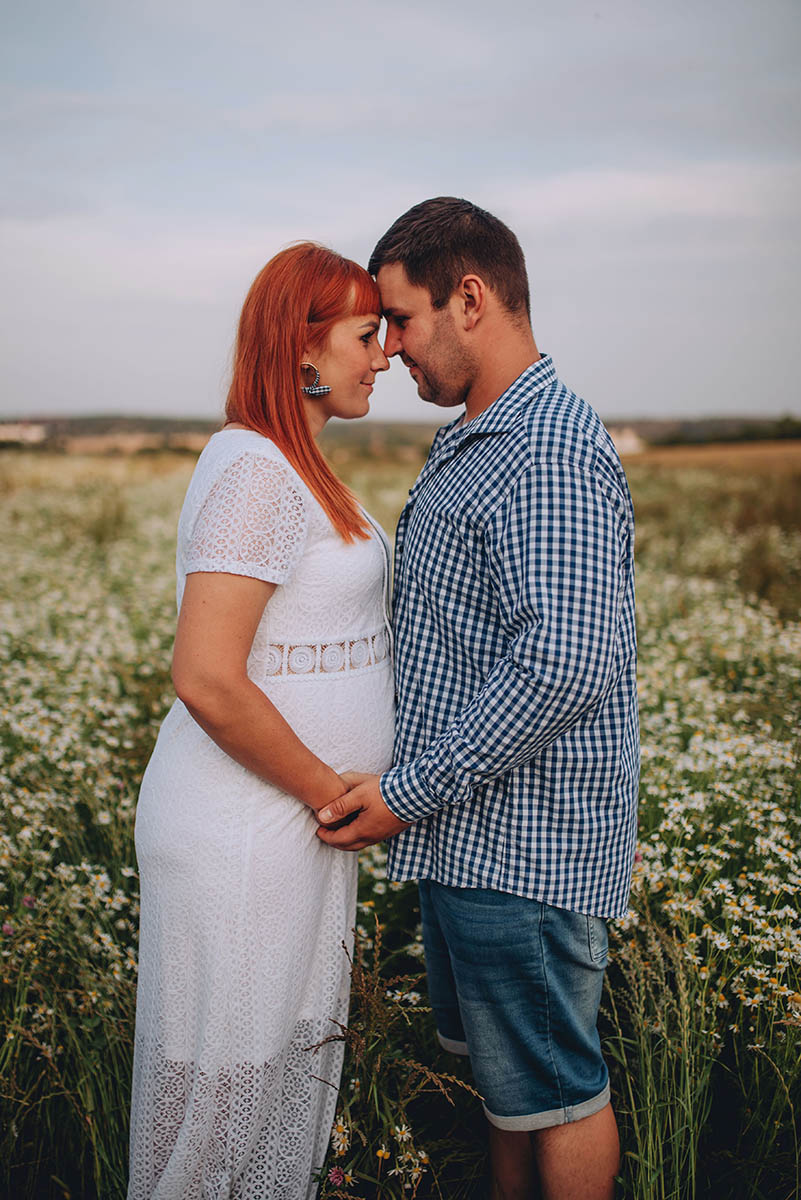 Muž s těhotnou partnerkou spojili čela na rozkvetlé louce.