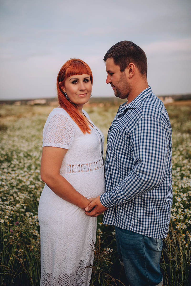 Muž se kouká na svou těhotnou partnerku na rozkvetlé louce.