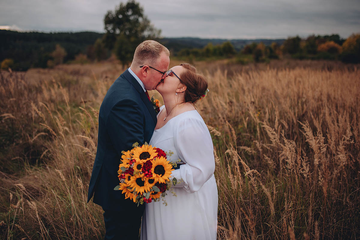 Novomanželský polibek na louce v podzimním prostředí.